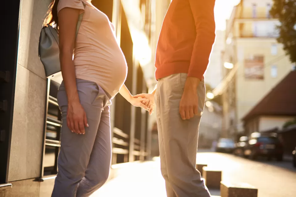A pregnant woman holds hand with a man in an urban setting.